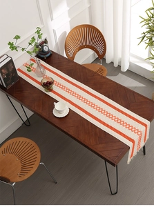 Detail of beige table runner with orange geometric patterns and tassel fringe on wood