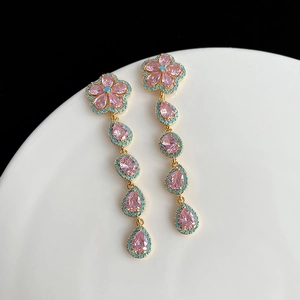 Détail de boucles d'oreilles dorées avec fleurs roses et perles turquoises sur un plateau blanc