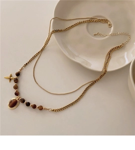 Flat lay of double-layer gold necklace with tiger eye beads and oval cross pendant