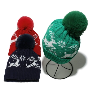 Close-up of knit Christmas hat featuring reindeer patterns and soft fluffy pom-poms
