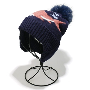 Kids shark winter hat with blue knit patterns, ear flaps and a fluffy faux fur pompom