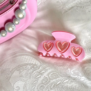 Pink heart-shaped Y2K hair claw clip with glossy finish on a white lace background