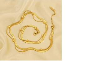 Makro-Detail einer goldenen zweilagigen Schlangenkette auf eleganter beige Seide