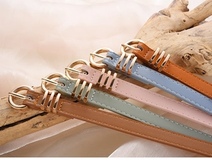 Detail of colorful slim faux leather belts with gold buckles on silk and wood