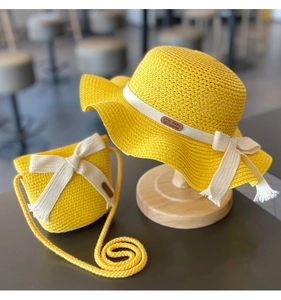 Detail of yellow straw sun hat and matching crossbody bag set with white ribbon bow