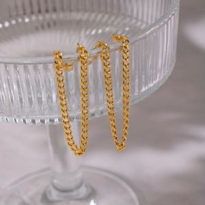Détail de boucles d'oreilles en maille gourmette dorée sur un verre texturé