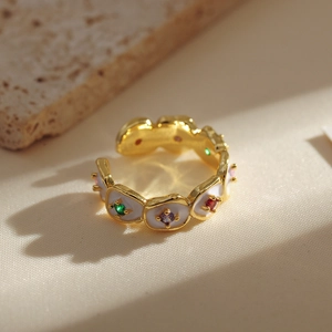 Macro detail of golden flower ring with white enamel and colorful gemstone accents