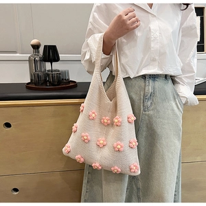 Detail of beige knitted tote bag with 3D pink flowers held by a model in casual setting