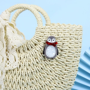 Handmade acrylic penguin brooch with red scarf on a beige straw bag, stylish accessory