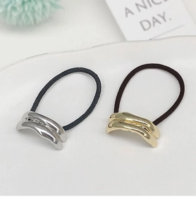 Detailed macro view of minimalist gold and silver metallic curved ponytail holders in a tray