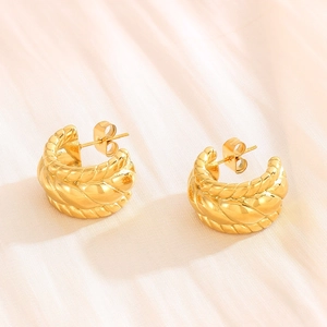 Detailed close-up of gold-plated twisted C-shaped earrings on soft beige fabric