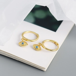 Close-up of gold hoop earrings with blue devil eye charms on a soft book background