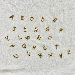 Golden stainless steel A-Z alphabet pendant set for DIY necklaces on beige linen background