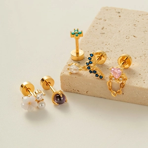 Golden cartilage piercings set with colorful zircon stones and chains on stone blocks