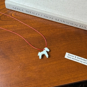 Detail of a cute white pony pendant on a red cord over a rustic wooden desk and book
