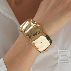 Close-up of wide gold cuff bracelet featuring irregular textured ripples and mirror finish