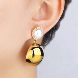 Close-up of model wearing gold polished metal ball earrings with a white pearl stud
