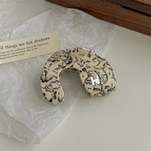 Detail view of marble pattern C-shaped hair clip with silver H letter and crystal