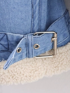 Close-up of blue denim jacket showing off-white fleece lining and silver metal buckles
