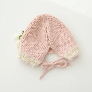 Close-up of pink knit baby bonnet featuring delicate lace trim and knit flower details