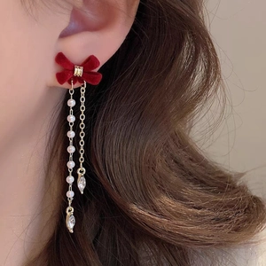 Detail of red velvet bow earrings with gold tassels, pearls and zircon on model ear