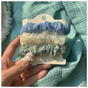 Close-up of three floral mesh scrunchies in blue and cream on white display card