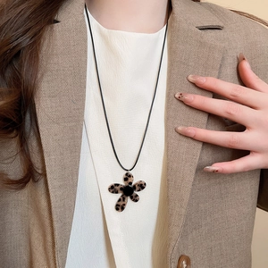 Close-up of leopard print flower pendant necklace worn with a brown blazer and white shirt