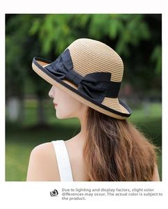 Detail of a beige woven straw hat featuring a wide brim and a large black bow ribbon