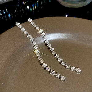 Macro shot of silver tassel earrings with square-cut rhinestones on a textured plate