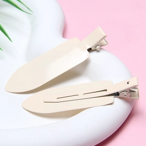 Pair of beige seamless hair clips with a smooth glossy finish on a decorative wavy base