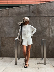 Close-up of white hollow-out knit cardigan and matching shorts in outdoor street setting