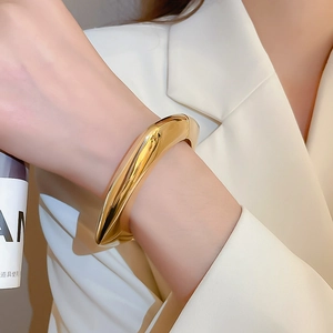 Detail of chunky gold wavy bangle with high-shine polished finish on female model