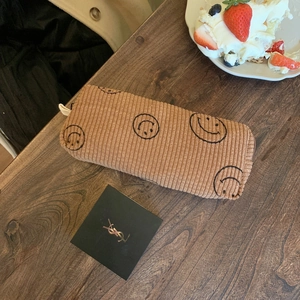 Detailed close-up of brown corduroy cosmetic bag with smiley face print on wood table