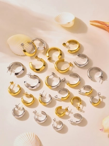 Detailed collection of shiny gold and silver C-shape hoop earrings on stone background