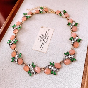 Detail of vintage gold necklace with pink resin gem and green leaf stones in wooden box