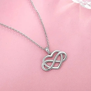 Macro shot of silver infinity heart pendant on a soft pink textured background