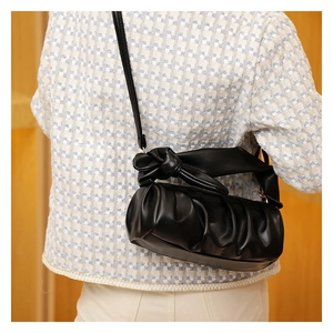 Detail of black pleated cloud bag with stylish knot strap design on a female shoulder
