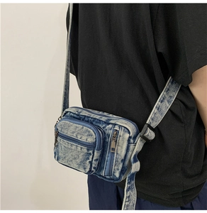 Detail showing washed denim crossbody bag with adjustable strap and metal zippers