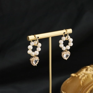 Elegant gold heart pearl earrings on a display stand against a black background