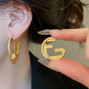 Macro detail of F-shaped golden hoop earring with sparkling pavé crystals and premium finish