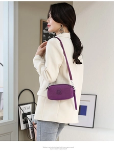 Purple nylon crossbody bag with multi-zipper compartments shown on model in modern room