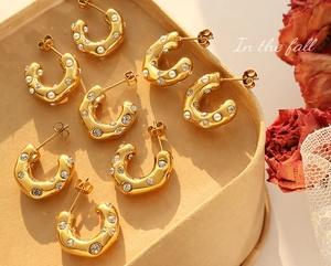 Detailed close-up of C-shaped gold-plated earrings with pearls and zircons in a gift box