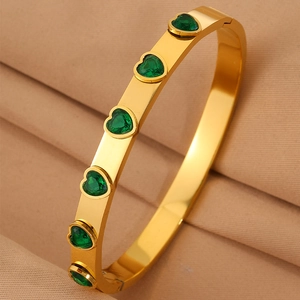 Gros plan d'un bracelet en acier doré orné de zircons verts en forme de cœur