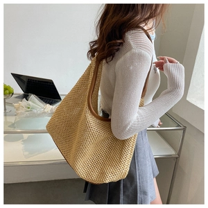 Detail of beige woven tote bag with brown faux leather shoulder strap worn by model