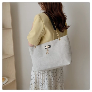 Detail of beige nylon tote bag with black faux leather strap and golden deer charm accent
