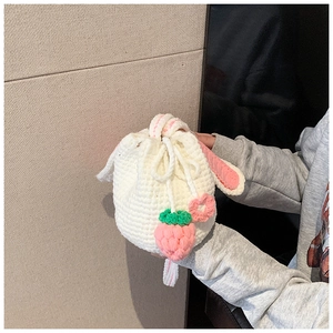 Detail of a handmade white crochet bucket bag featuring pink bunny ears and strawberry charm