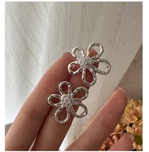 Detail view of silver flower earrings with textured petals and sparkling zircon center