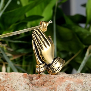 Titanium steel praying hands pendant in gold finish hanging on a natural branch