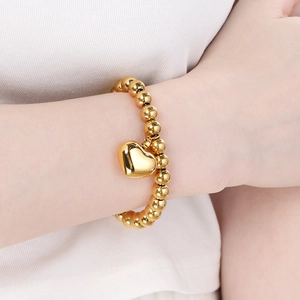 Close-up of a 18K gold plated beaded bracelet featuring a polished heart pendant on a wrist