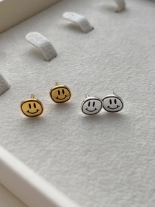 Détail de boucles d'oreilles smiley en argent et or dans un écrin à bijoux blanc